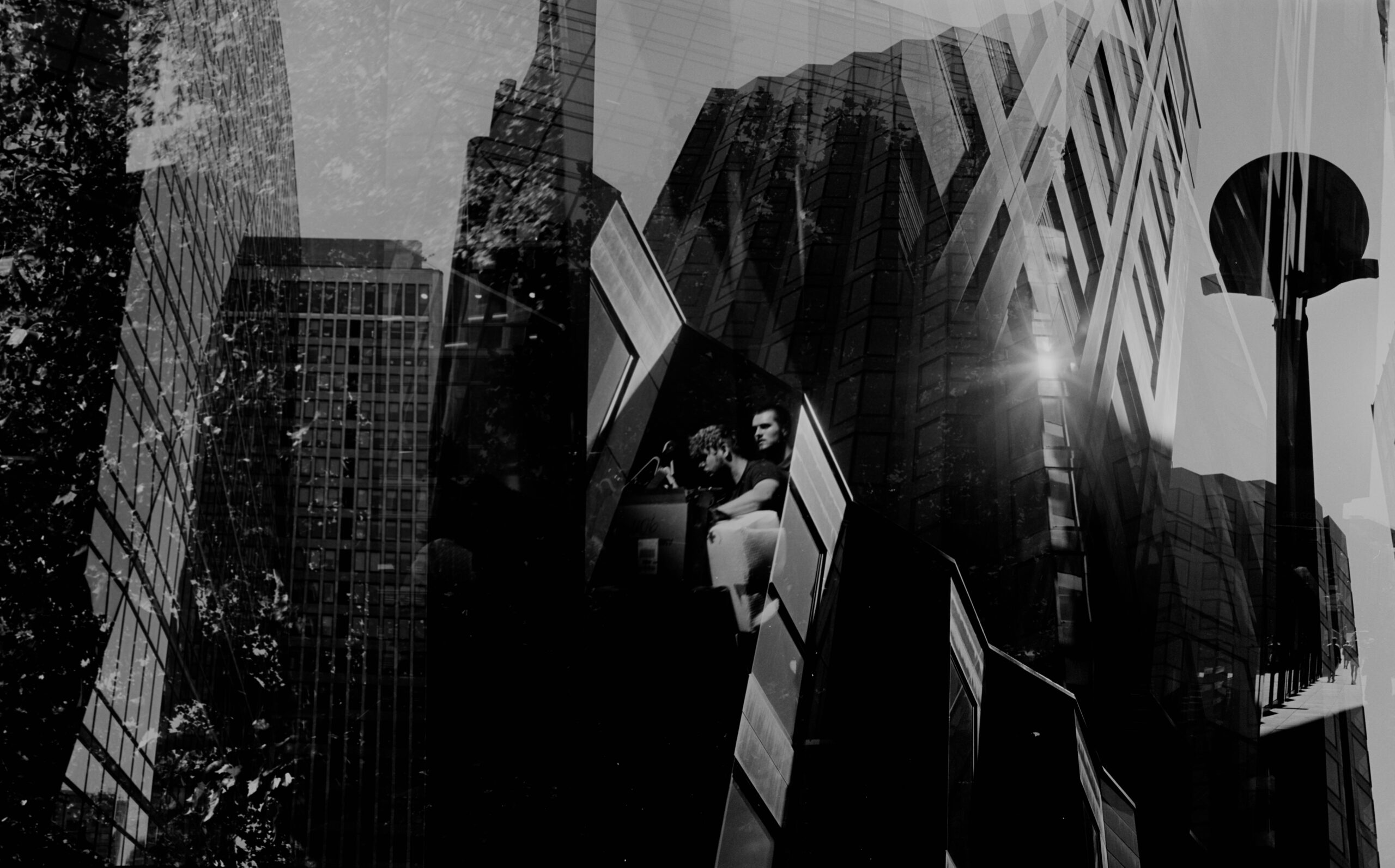 Black-and-white urban double exposure with glass buildings and sun flare